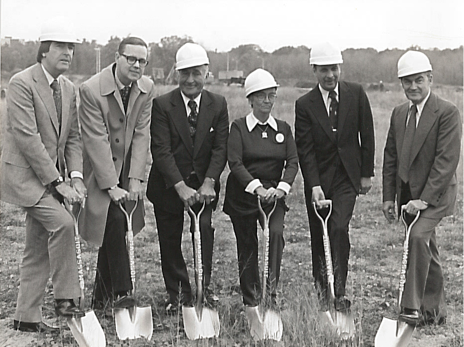 Six people with hard hats on holding shovels into the ground at a groundbreaking.