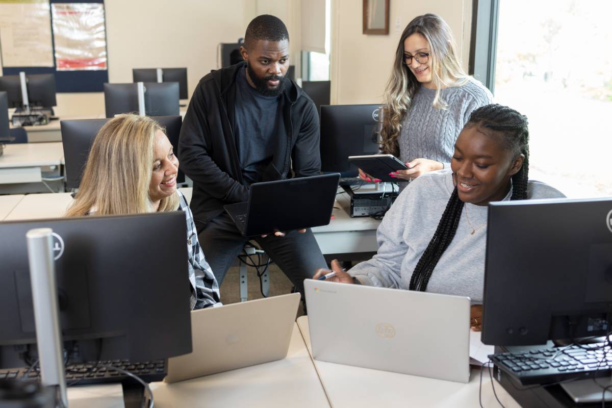 Four students talking while sitting in a computer lab.