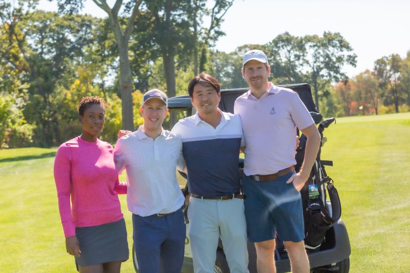 Group of people smiling standing at a golf course.