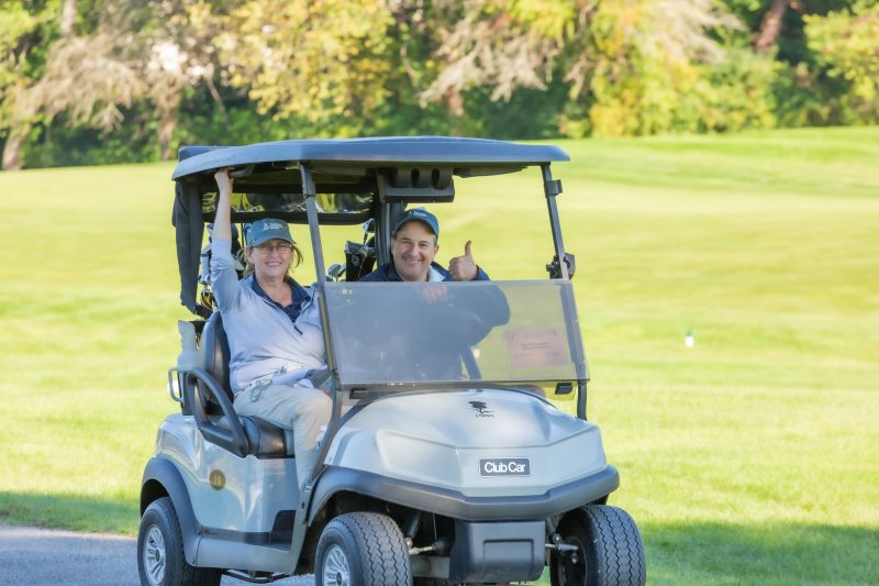Two people smiling riding in a golf cart.