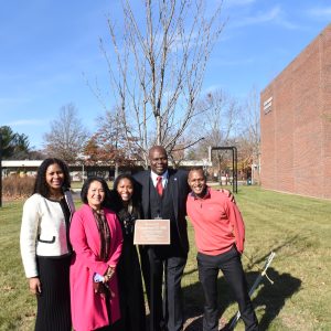 Pamerson Ifill '89 stands with three family members at a tree planted in his honor at Massasoit Community College near the Field House.