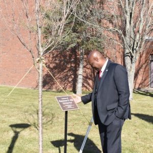 Ifill leaning down to read the plaque dedicating a tree in his honor at Massasoit.