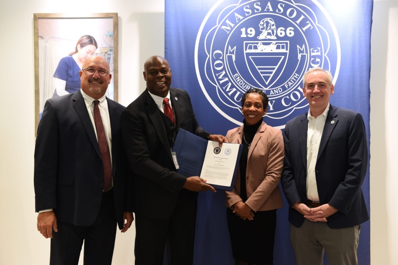 Massasoit Interim President Mitchell, Commissioner of Probation Ifill, Associate Vice President for the Future of Work Institute Sauvignon, and Labor and Workforce Development Undersecretary Cutler standing together in front of the Massasoit seal with a newly signed MOU at an Open House for the Future of Work Institute on Nov. 14, 2024.